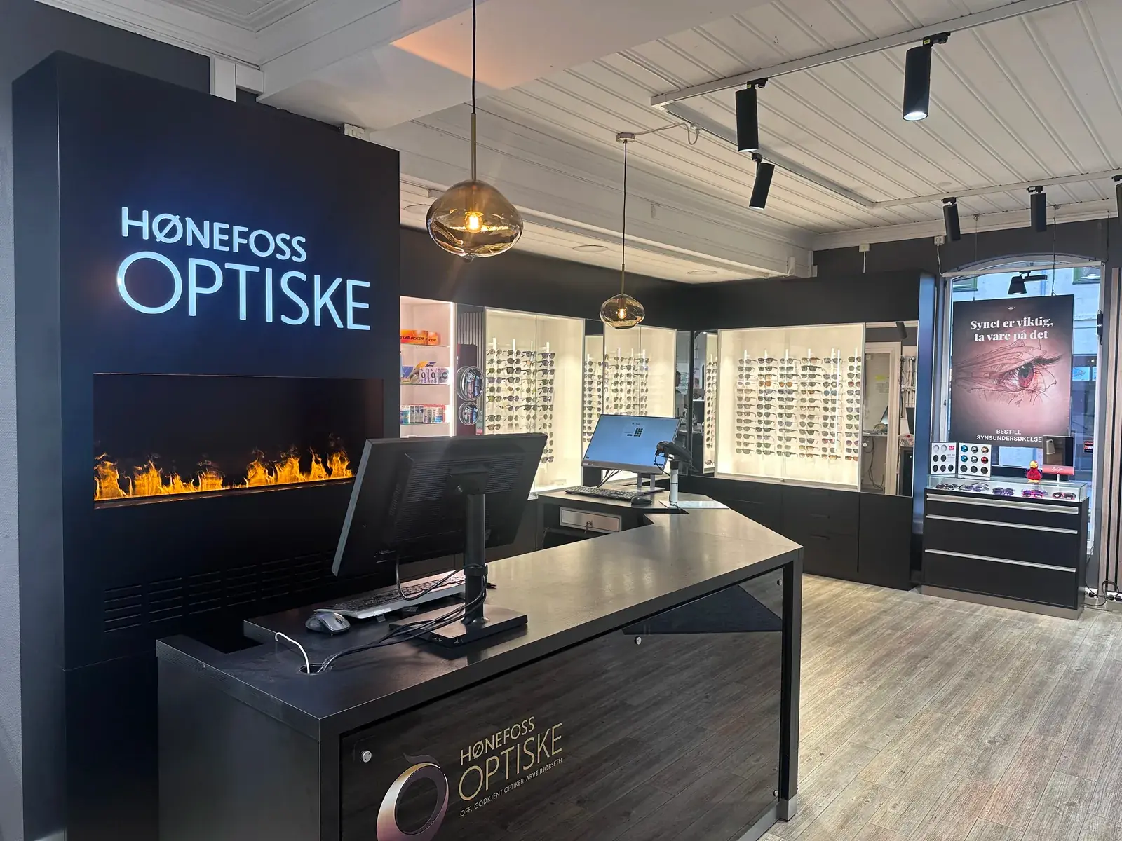 Disken i Hønefoss Optiske med opplyst logo, peis og brillevegger i bakgrunnen